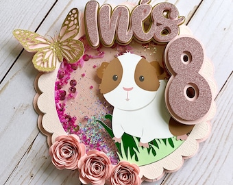May include: A pink and gold cake topper with a guinea pig, a butterfly, and the text "Mia's 8".