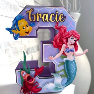 May include: A white ceramic mug with a black handle and the text "But First, Coffee" in a handwritten style. The mug is on a white surface. The mug is approximately 4 inches tall.