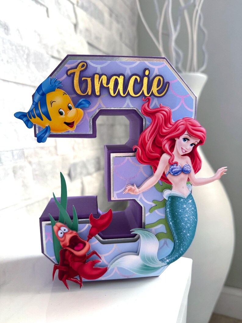 May include: A white ceramic mug with a black handle and the text "But First, Coffee" in a handwritten style. The mug is on a white surface. The mug is approximately 4 inches tall.