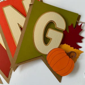 May include: A green, brown, and orange paper banner with the word "GIVING" in large, cream-colored letters. The "G" is highlighted with a pumpkin, fall leaves, and a brown twine string.