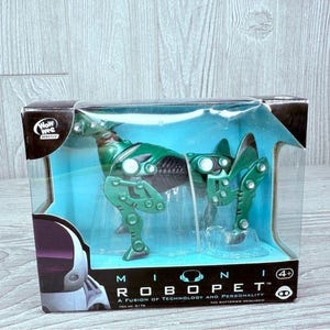 May include: Green robotic toy in a clear plastic box with the words "Mini Robopet" and "A Fusion of Technology and Personality" on the box. The toy is a robot dog with a green and black body and a silver head.