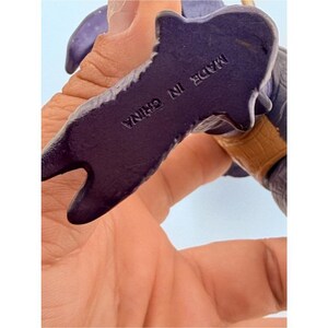 May include: A purple plastic action figure foot with a textured surface and a tan-colored band around the ankle area. The bottom of the foot is clearly embossed with the text MADE IN CHINA in capital letters, indicating the country of origin.