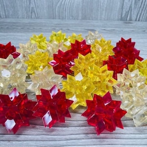 May include: A collection of red, yellow, and clear plastic star-shaped ornaments. The ornaments are arranged in a random pattern on a wooden surface.