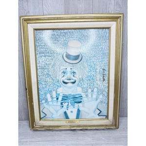 May include: A framed painting of a clown wearing a top hat and a bow tie, depicted in shades of blue and white. The clown is shown with hands raised, holding blue string. The artwork is enclosed in a gold-toned frame with a light-colored inner border.