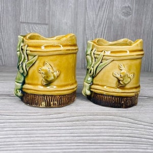 May include: Two small ceramic planters with a bamboo design and frog accents. The planters are brown, yellow, and green.