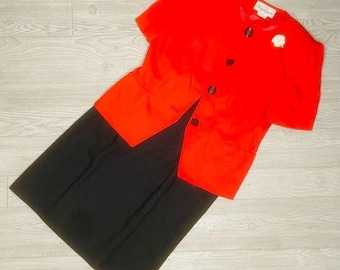 May include: A red short-sleeved jacket with a black skirt. The jacket has a button closure and a white flower embellishment. The text "City Chic" is visible on the jacket.