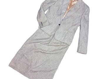 Puede incluir: Un traje de falda a rayas grises y blancas. El traje incluye una blazer con un solo botón y una falda a juego hasta la rodilla. La blazer tiene tres botones en cada puño y dos bolsillos delanteros. El forro interior de la blazer es de color melocotón claro.