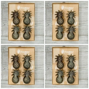 Puede incluir: Cuatro juegos de tres tiradores de cajón de piña dorados en una caja marrón con el texto "Embellished Home" en la parte delantera.