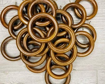 Könnte beinhalten: Ein Stapel brauner Holz-Vorhangringe mit silbernen Haken. Die Ringe sind übereinander gestapelt und alle gleich groß.