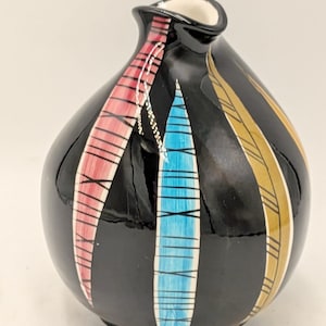 May include: A small, bulbous black ceramic vase featuring a glossy finish and a narrow neck. The exterior is decorated with three vertical, elongated leaf-shaped patterns in pink, bright blue, and mustard yellow, each accented with thin black cross-hatching.