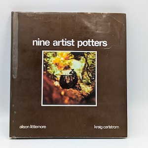 May include: A brown book cover with the title "nine artist potters" in white text. The cover features a photograph of two brown ceramic pots in a woodland setting. The authors' names, Alison Littlemore and Kraig Carlstrom, are listed below the photograph.
