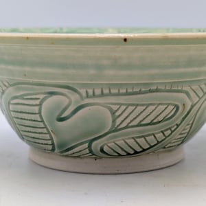 May include: A pale green ceramic bowl with a wide rim and a footed base. The bowl features a heart-shaped design with diagonal lines. The bowl is approximately 20 cm in diameter.