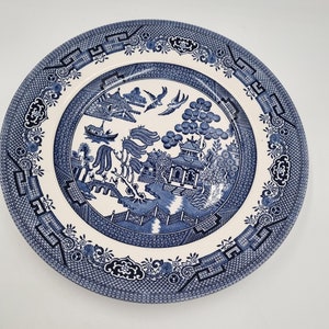 May include: A blue and white ceramic dinner plate featuring a traditional Chinese willow pattern. The plate depicts a detailed design of a pagoda, willow trees, birds, and a boat.