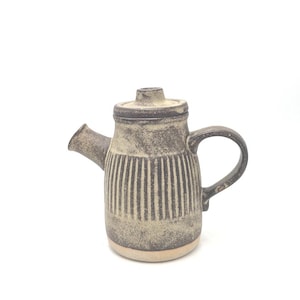 May include: A ceramic teapot with a lid, spout, and handle. The teapot is a mottled beige and brown colour with vertical striped detailing on the body. The base is a lighter beige colour.