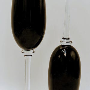 May include: Two wine glasses, one upright and one inverted, against a white backdrop. The bowls are a deep black, contrasting with the clear stems and bases. The glasses are designed for wine.