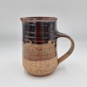 May include: A brown and black ceramic jug with a textured surface. The jug has a handle and a spout.