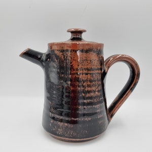 May include: A black and brown ceramic teapot with a lid. The teapot has a textured surface and a handle.