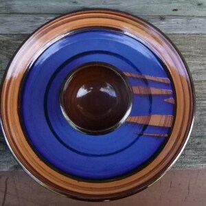 May include: A ceramic serving dish with a brown central bowl, surrounded by a blue interior and a brown and orange rim. The blue section has brown stripe accents. The dish is circular and appears handmade.