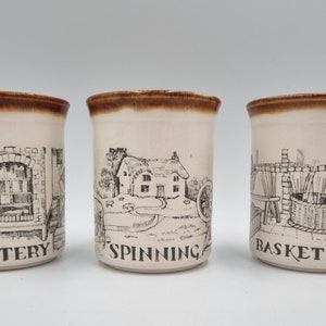 May include: Three ceramic mugs with brown rims and black and white illustrations. The mugs depict scenes of pottery, spinning, and basket making.