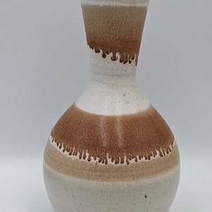 May include: A white ceramic vase with brown and beige stripes. The vase has a wide base and a narrow neck.