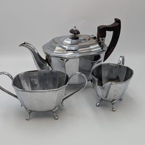 May include: A silver teapot, sugar bowl, and creamer set with a wooden handle on the teapot.