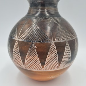 May include: A brown ceramic vase with a geometric pattern carved into the surface. The vase has a rounded body and a narrow neck.