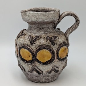 May include: A small, white ceramic jug with a brown handle and yellow and brown geometric designs.