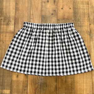 May include: A black and white checkered skirt with an elastic waistband. The skirt is made of a lightweight fabric and has a classic gingham pattern. The skirt is a mini skirt style.
