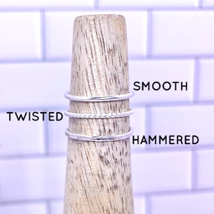 May include: Three silver rings on a wooden display stand. The rings are labeled "Smooth", "Twisted", and "Hammered". Listing is for one ring.