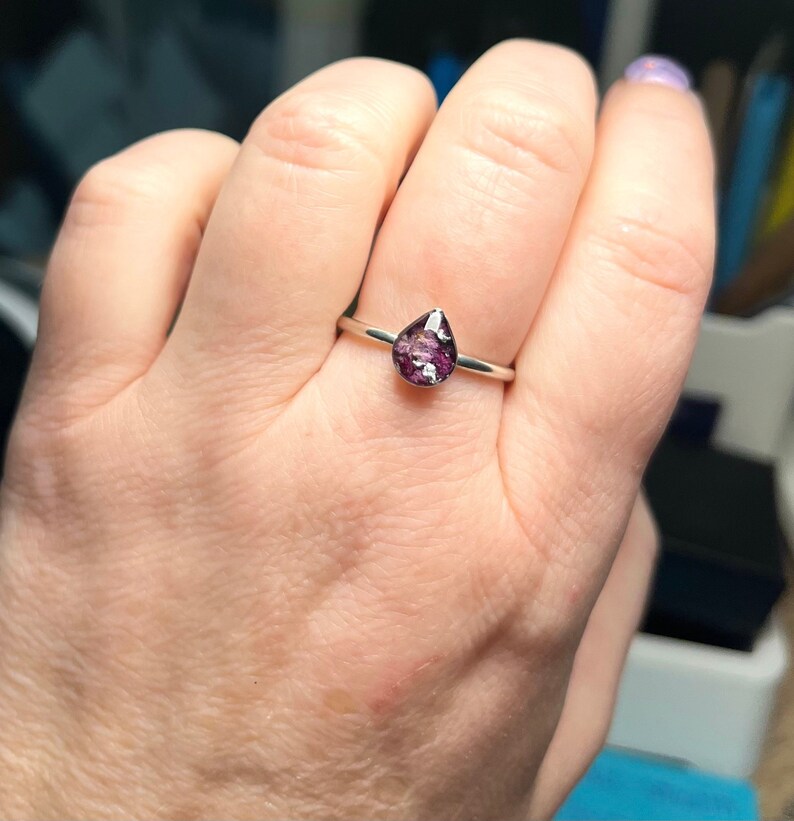 K&ouml;nnte beinhalten: Ein silberner Ring mit einem tropfenf&ouml;rmigen violetten Stein.