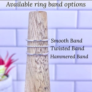 K&ouml;nnte beinhalten: Drei silberne Ringe auf einem Holzst&auml;nder. Die Ringe sind mit "Smooth Band", "Twisted Band" und "Hammered Band" beschriftet.
