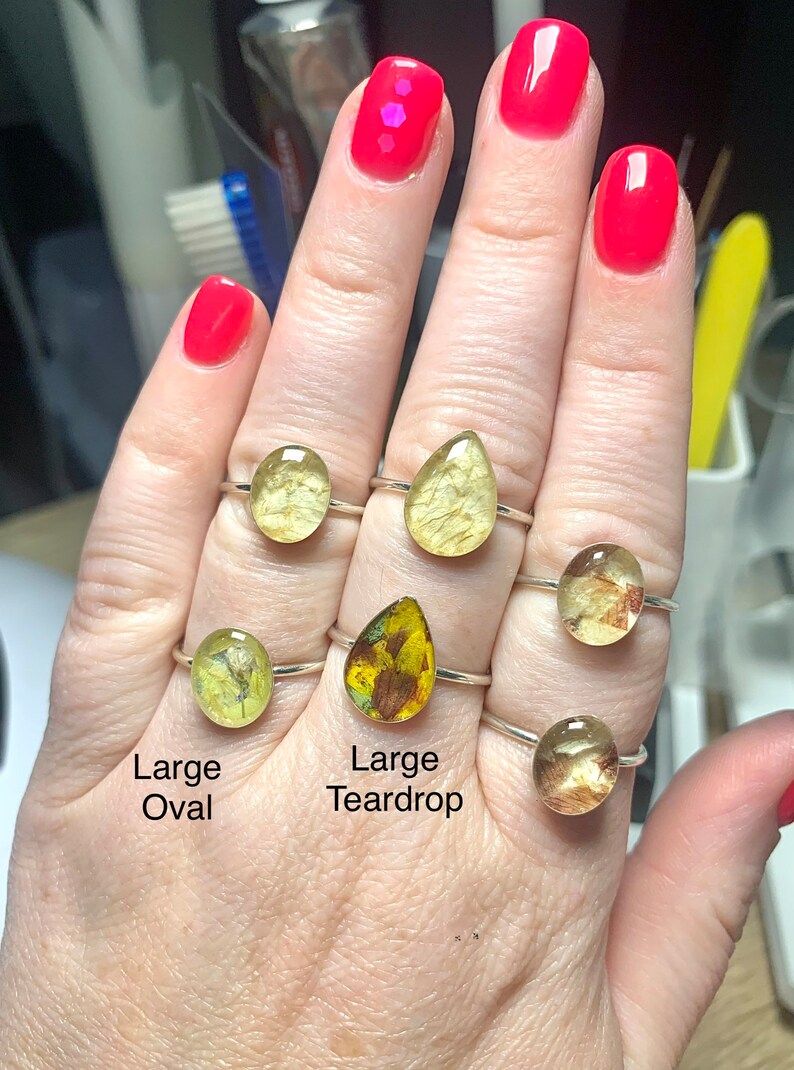 K&ouml;nnte beinhalten: F&uuml;nf Silberringe mit unterschiedlich geformten Harzsteinen. Die Steine sind klar und enthalten gepresste Blumen und Bl&auml;tter. Die Ringe sind mit "Large Oval" und "Large Teardrop" beschriftet.