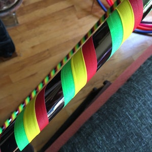 Pu&ograve; includere: Un hula hoop circolare caratterizzato da una base in metallo argentato riflettente. Il cerchio &egrave; avvolto in un motivo diagonale ripetitivo di nastro adesivo rosso vibrante, giallo brillante e verde lime, creando un'estetica colorata a spirale.