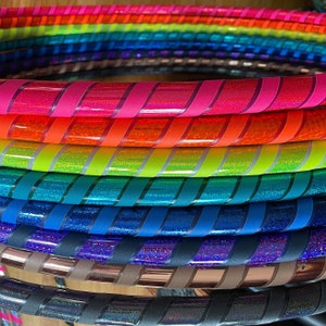 Può includere: Un mucchio di cerchi da hula a strisce colorate. I cerchi sono in plastica e hanno una varietà di colori, tra cui rosso, arancione, giallo, verde, blu, viola e rosa.