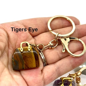 May include: A gold-tone handbag keychain with a tigers eye stone. The keychain has a gold-tone clasp and a gold-tone ring.