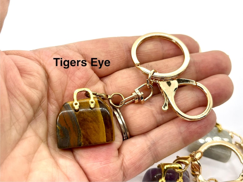 May include: A gold-tone handbag keychain with a tigers eye stone. The keychain has a gold-tone clasp and a gold-tone ring.
