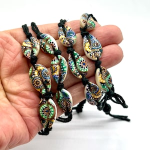 May include: A close-up of several strands of decorative beads. The beads are shell-shaped, with a cream base and colorful patterns in blue, green, yellow, and brown. The beads are strung on black cords.
