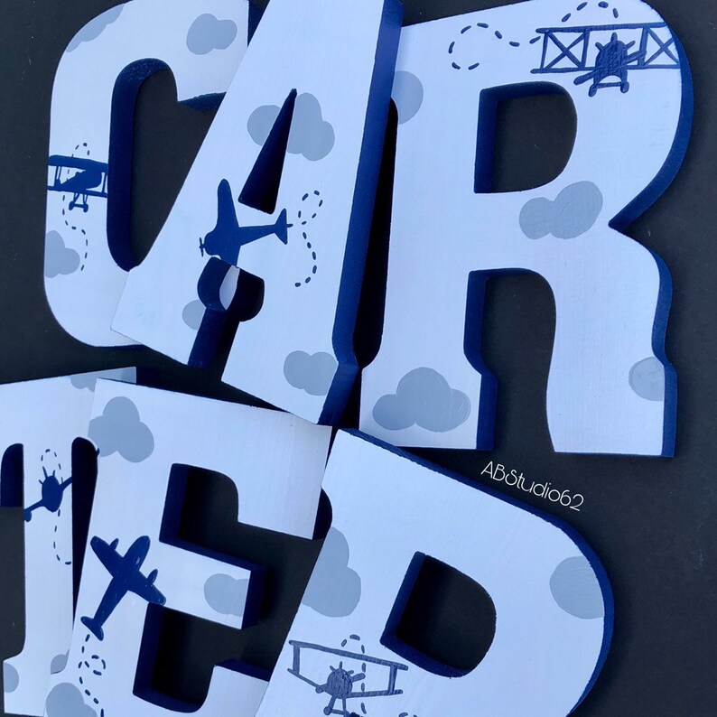 May include: White wooden letters spelling "CARTER" with blue trim and a blue airplane and gray clouds design.