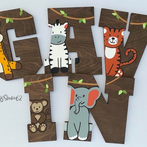 May include: Wooden letters spelling out the name "GAVIN" with a jungle theme. Each letter is painted brown and features a different animal: a giraffe, zebra, tiger, monkey, and elephant.