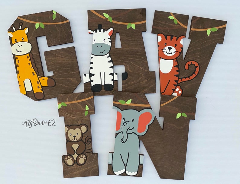 May include: Wooden letters spelling out the name "GAVIN" with a jungle theme. Each letter is painted brown and features a different animal: a giraffe, zebra, tiger, monkey, and elephant.