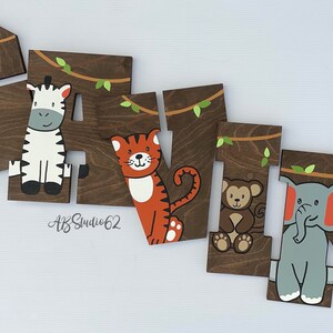 May include: Wooden letters spelling the name "Gavin" with a jungle theme. Each letter is painted brown and features a different animal: a giraffe, zebra, tiger, monkey, and elephant. The letters are decorated with green leaves and vines.