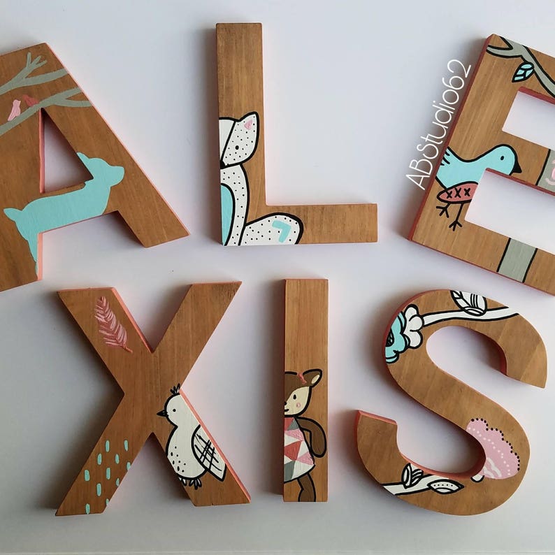 May include: Wooden letters spelling out the name "ALEXIS" painted in various colors with different animal and nature-themed designs. The letters are painted in shades of brown, pink, blue, and white.