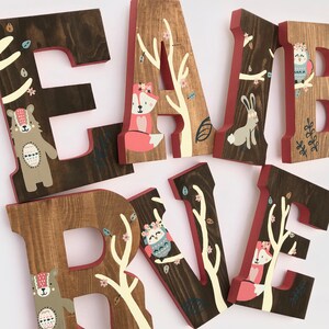 May include: Wooden letters spelling "EARL" and "IVE" with a woodland theme. Each letter is painted brown with white branches and pink flowers. The letters are decorated with painted animals including a fox, owl, bear, and rabbit.