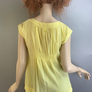 May include: A yellow, short-sleeved, lightweight, cotton blouse with a gathered waist and a scoop neckline.