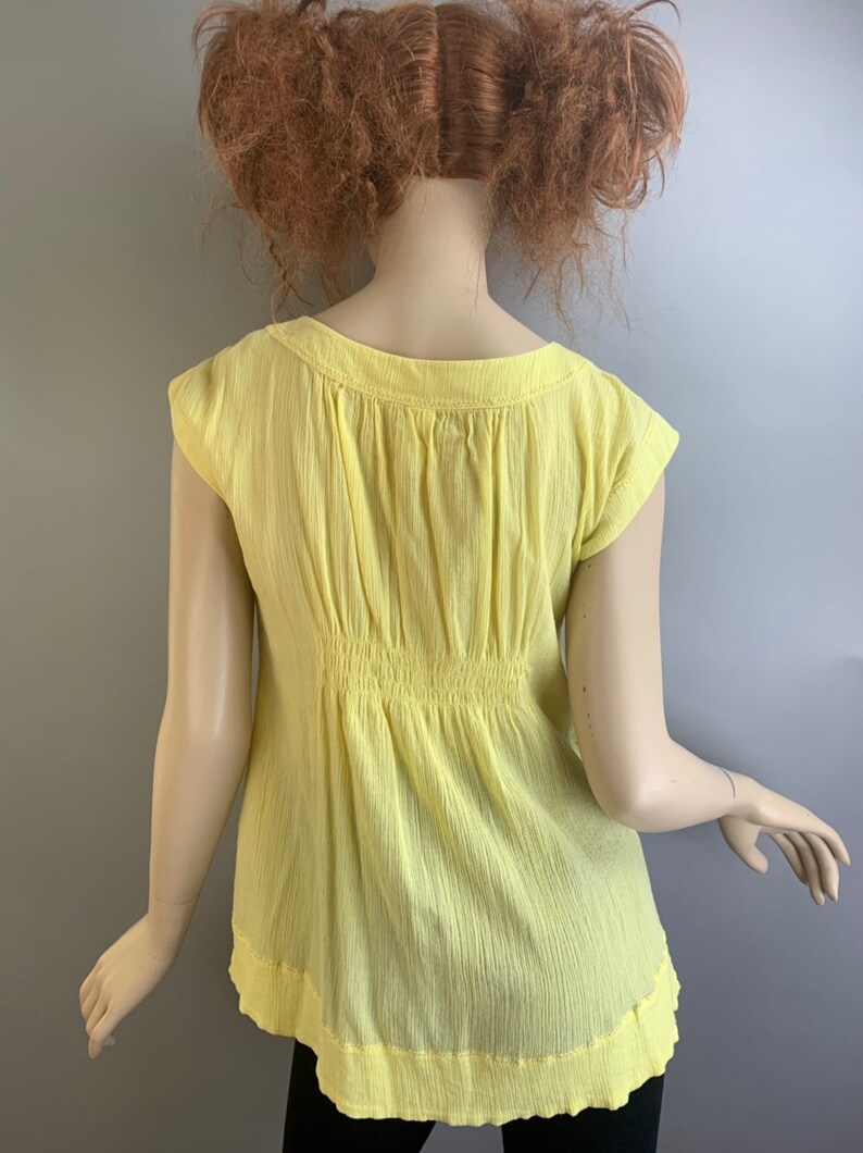 May include: A yellow, short-sleeved, lightweight, cotton blouse with a gathered waist and a scoop neckline.