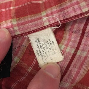 May include: A white care label with black text on a red and white plaid fabric. The text reads: "WPL150 POLYESTER 63% COTTON 33% MACHINE WASH AT MEDIUM TEMP. TUMBLE DRY AT MED. TEMP. HANG UP IMMEDIATELY. KOREA"