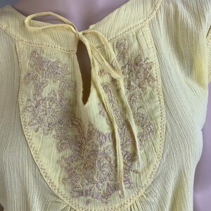 May include: A yellow cotton blouse with a keyhole neckline and gold embroidery. The blouse has a tie at the neckline.