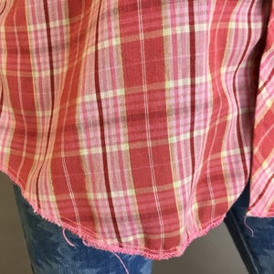 May include: A red and white plaid shirt with a pink seam. The shirt is frayed at the bottom edge.
