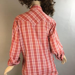 May include: A pink and white plaid long-sleeve shirt with a pointed collar and button closure. The shirt has a yoke in the back and a single button on each cuff.