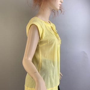 May include: A yellow sheer blouse with a tie at the neckline and embroidered details.